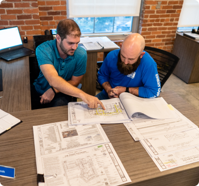 two men in the office working on some blueprint